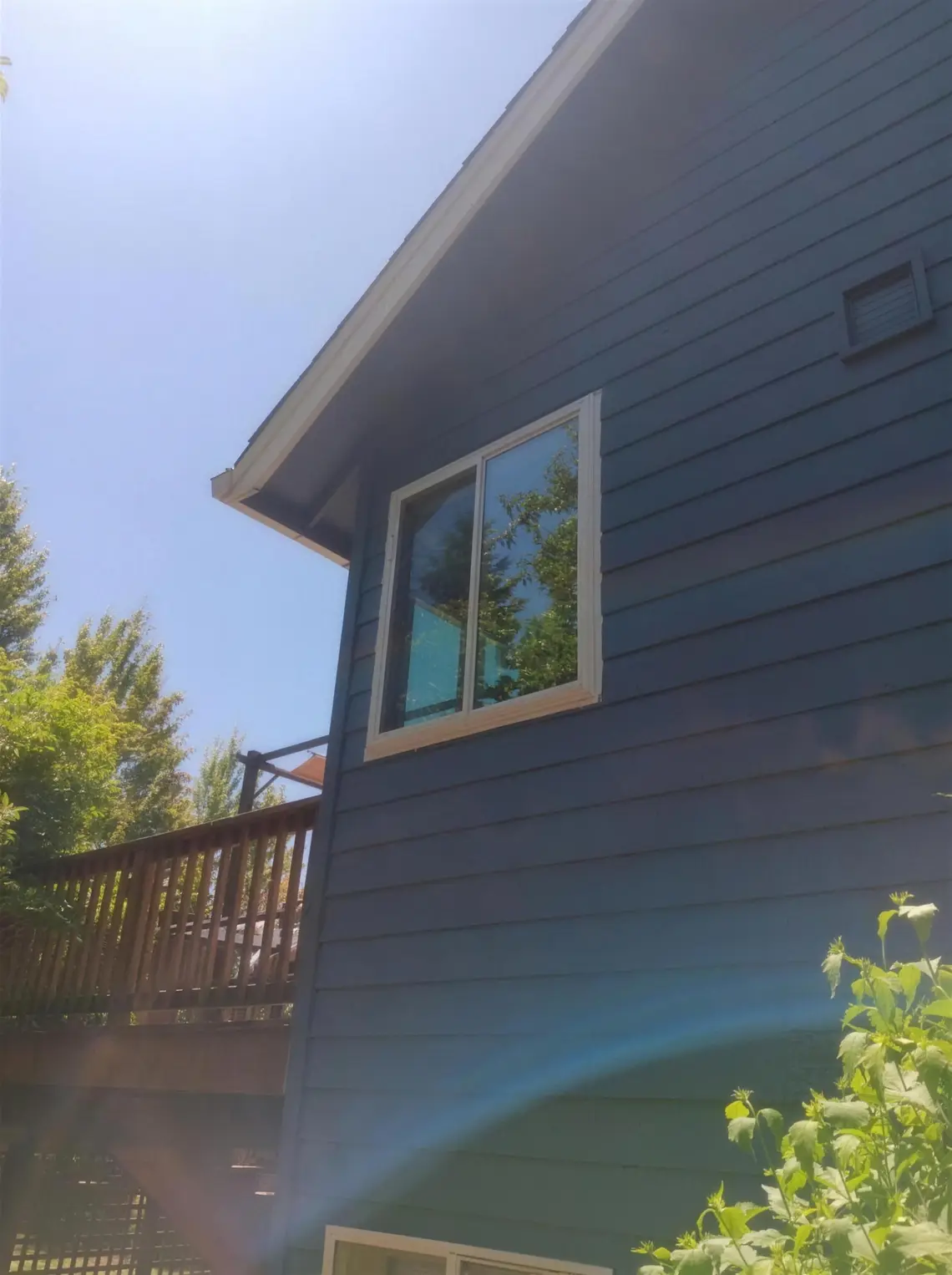 White slider window installed on a dark blue house beside a wood deck, showing a finished Clearview installation.