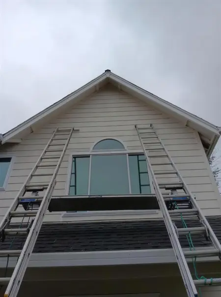 Two ladders set against a cream gable with an arched transom window mid-replacement