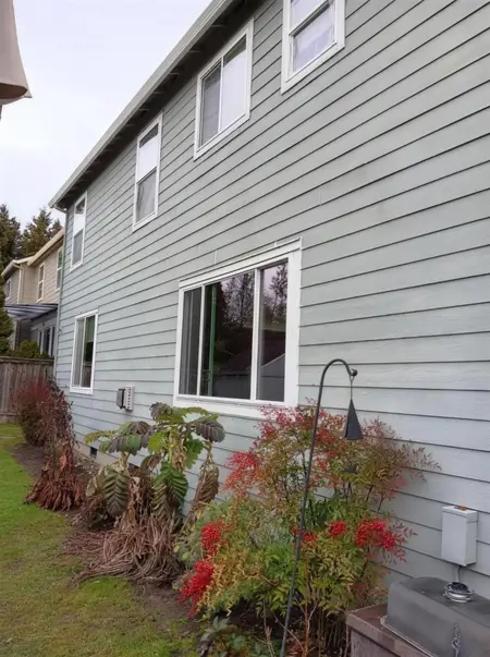Side elevation of a gray lap-siding house with a new white slider and upper windows