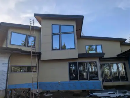 Multiple black-framed windows set into a modern new-construction home with tan panel siding and exposed weather barrier at the base