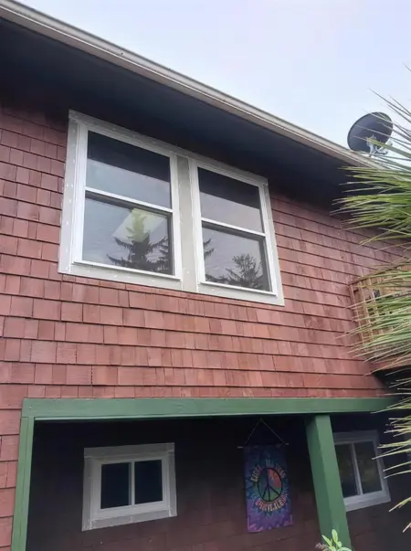 Two upper-story windows on a redwood shake house above a green porch beam