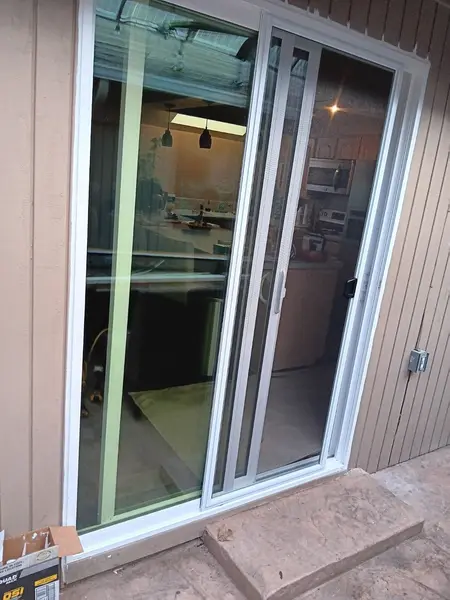 Finished sliding glass door with retractable screen on a tan house, kitchen visible through the glass