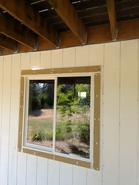 New white vinyl slider window with primed tan trim, seen from under a covered porch roof