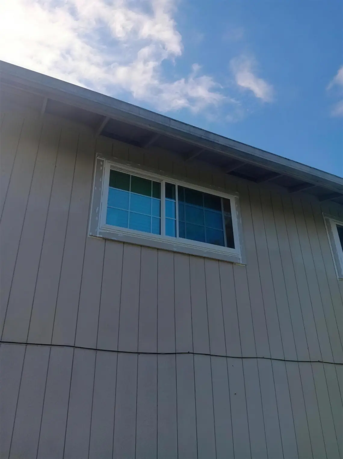 Close view of an upper-story white slider on tan vertical siding, showing the kind of opening where frame size and exposure matter.